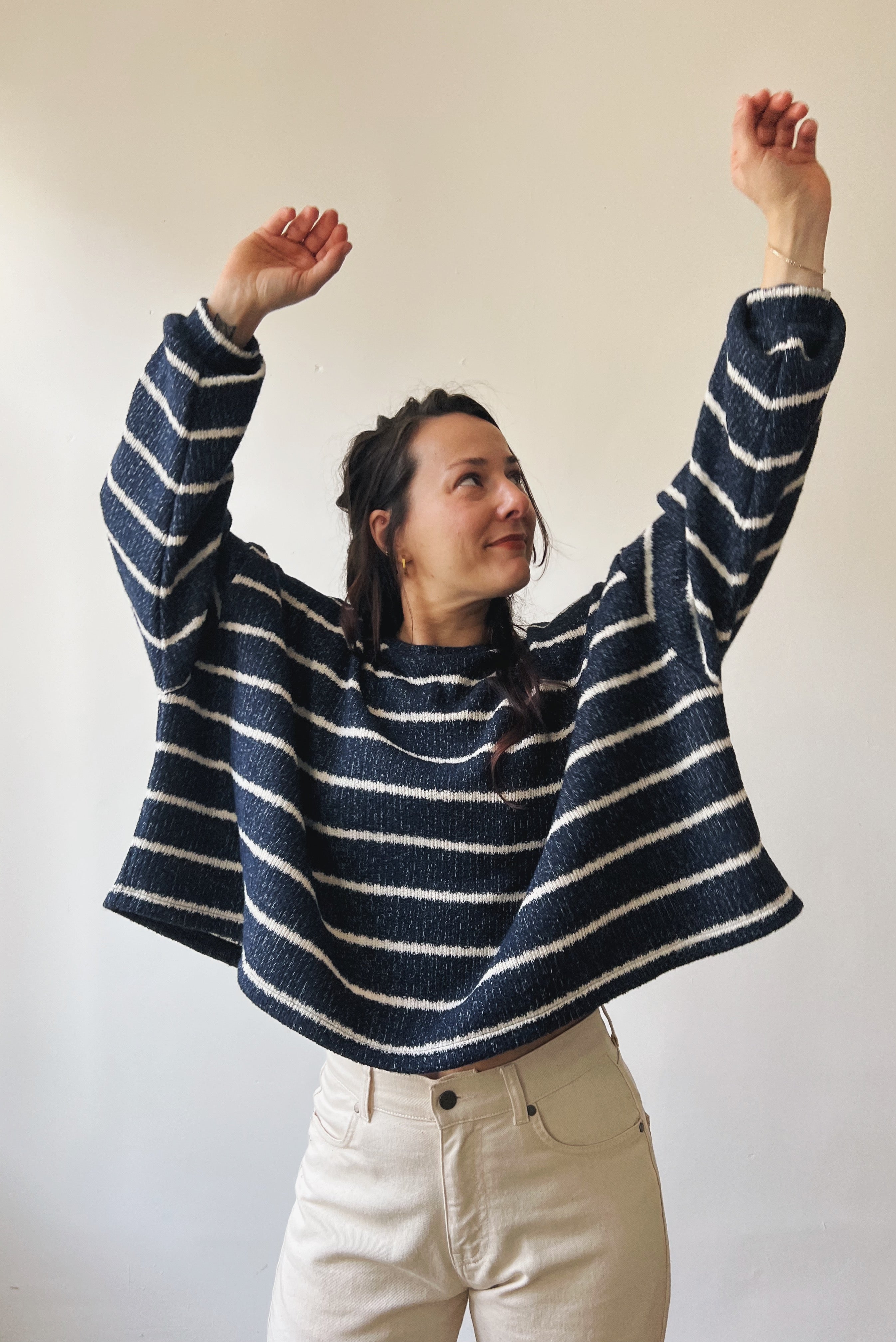Woman wearing a blue-white striped sweater with arms raised against a plain background