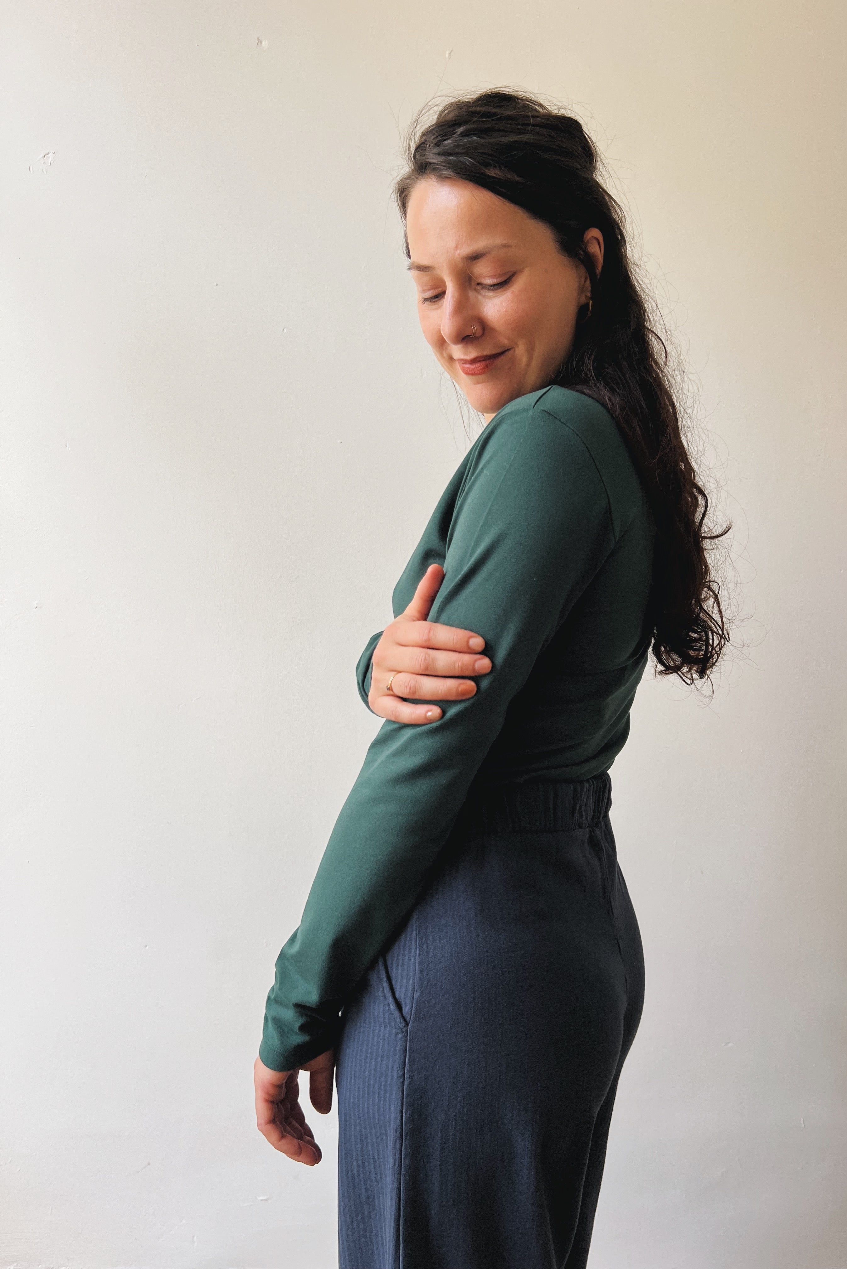 Woman wearing a pine long-sleeve  and dark blue pants against a plain background