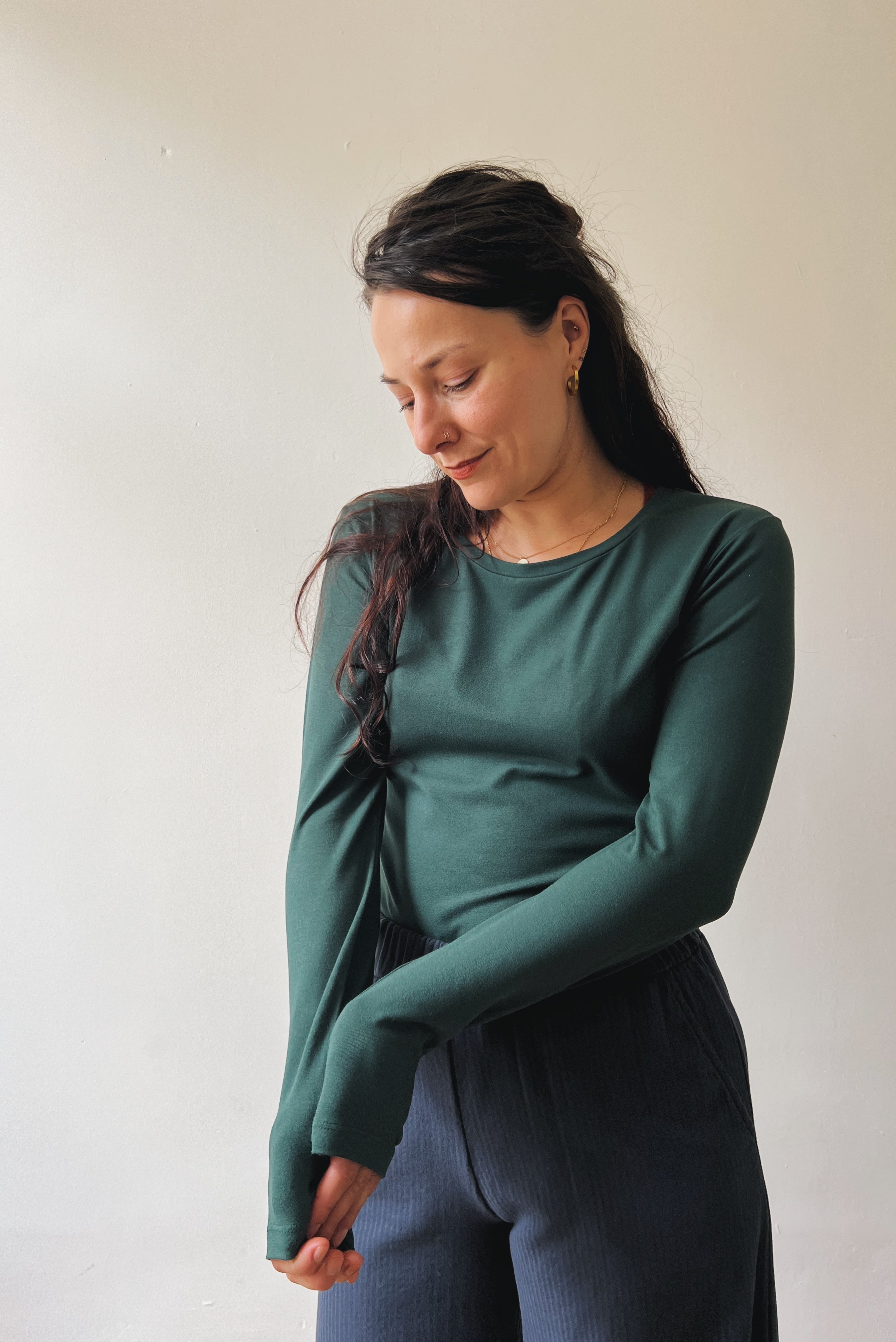 Woman wearing a pine long-sleeve  and dark blue pants against a plain background