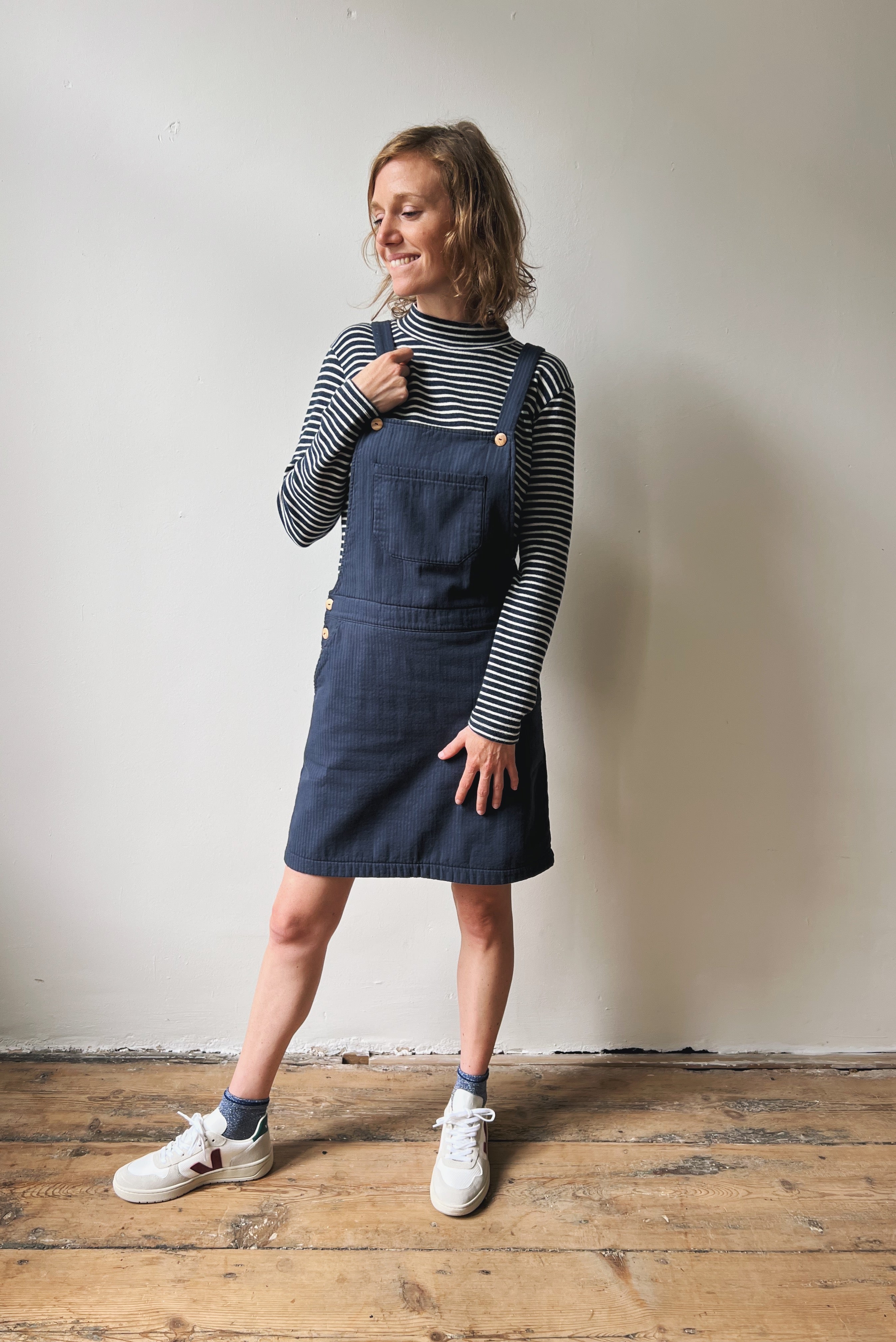 Woman wearing a blue-white striped turtleneck and blue salopettedress and white sneakers