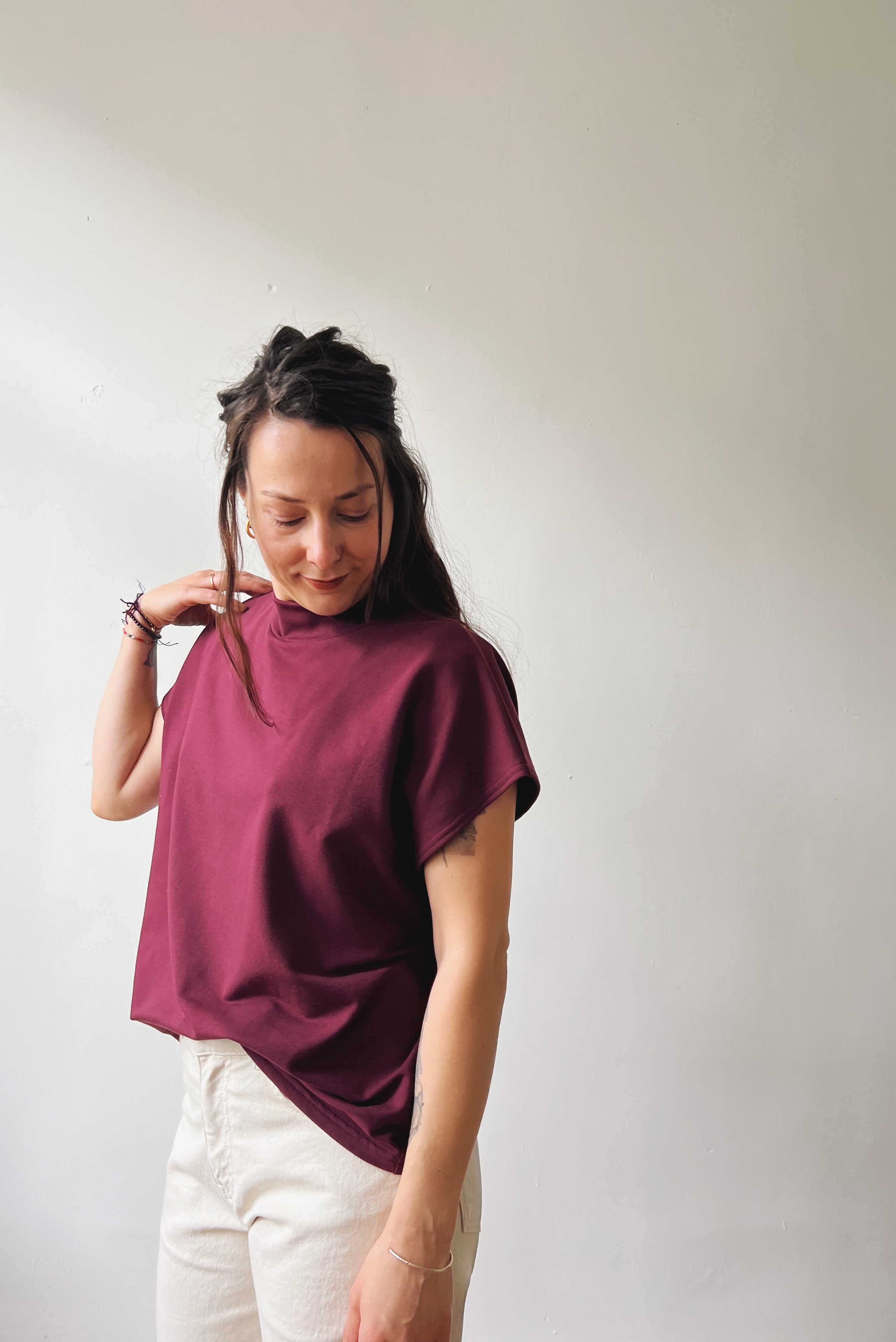 Woman wearing a aubergine sleeveless sweater and oat jeans against a plain background