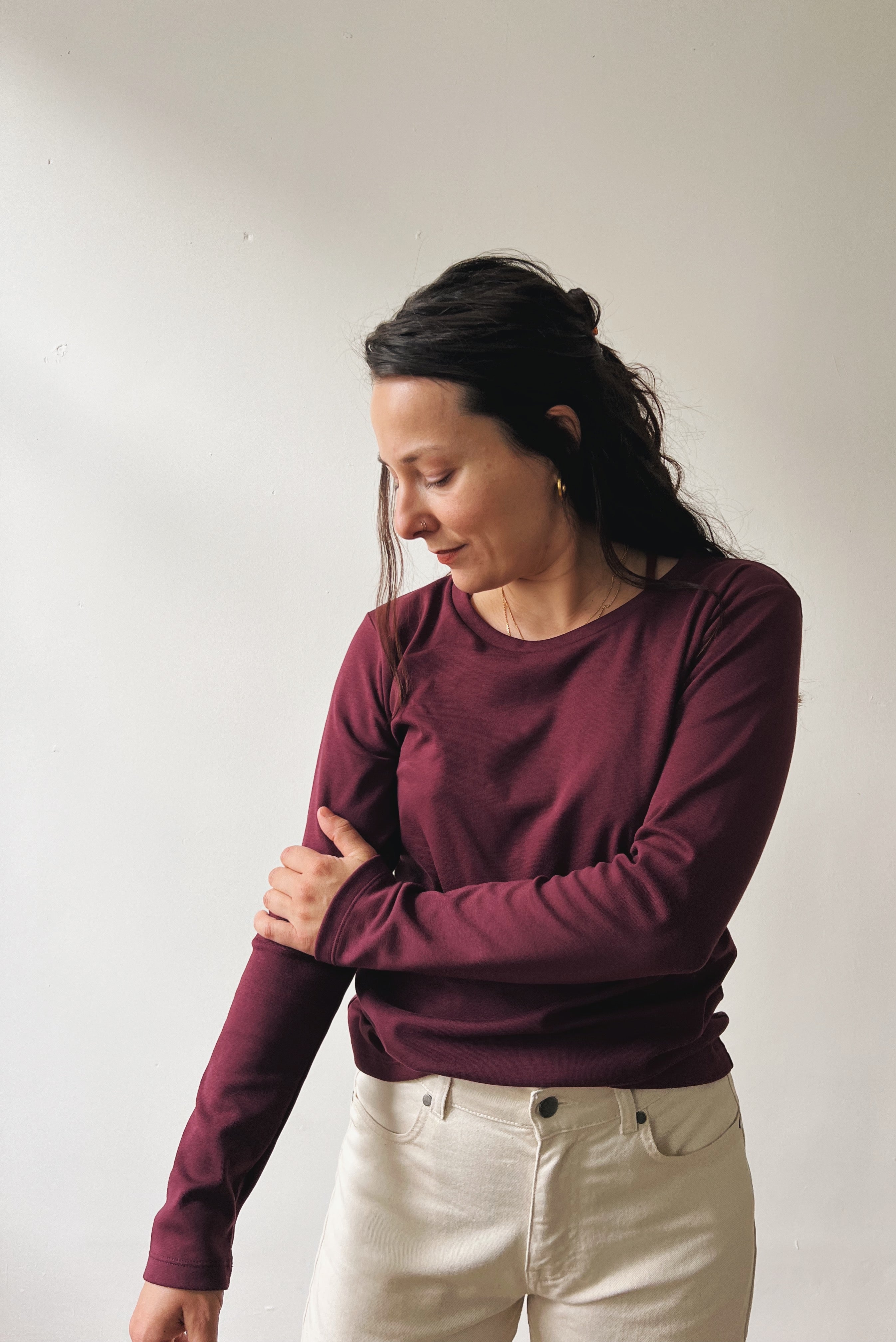 Woman wearing a aubergine long-sleeve shirt and oat boyfriend jeans against a plain background