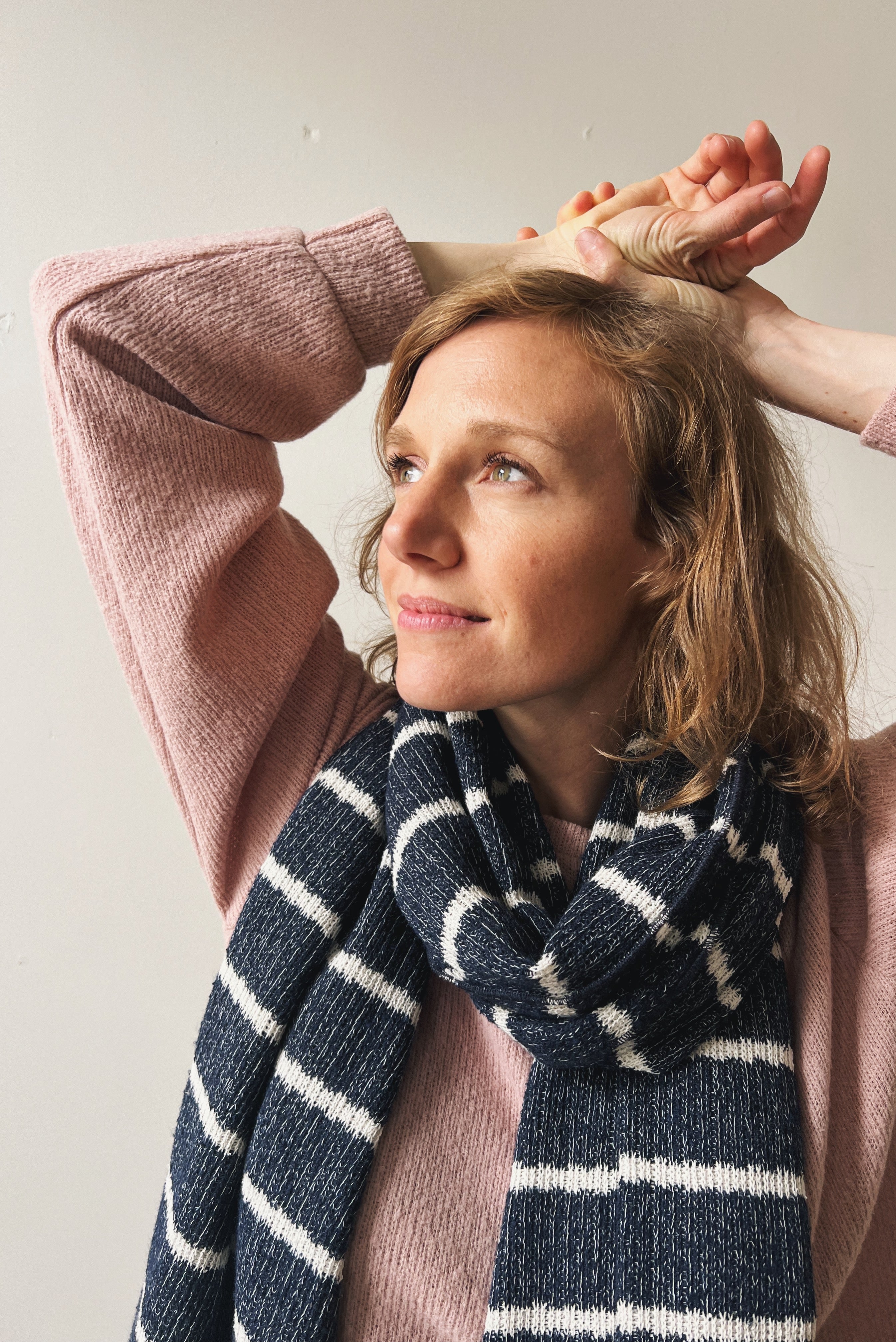 Woman wearing a pink sweater and blue striped scarf against a plain background