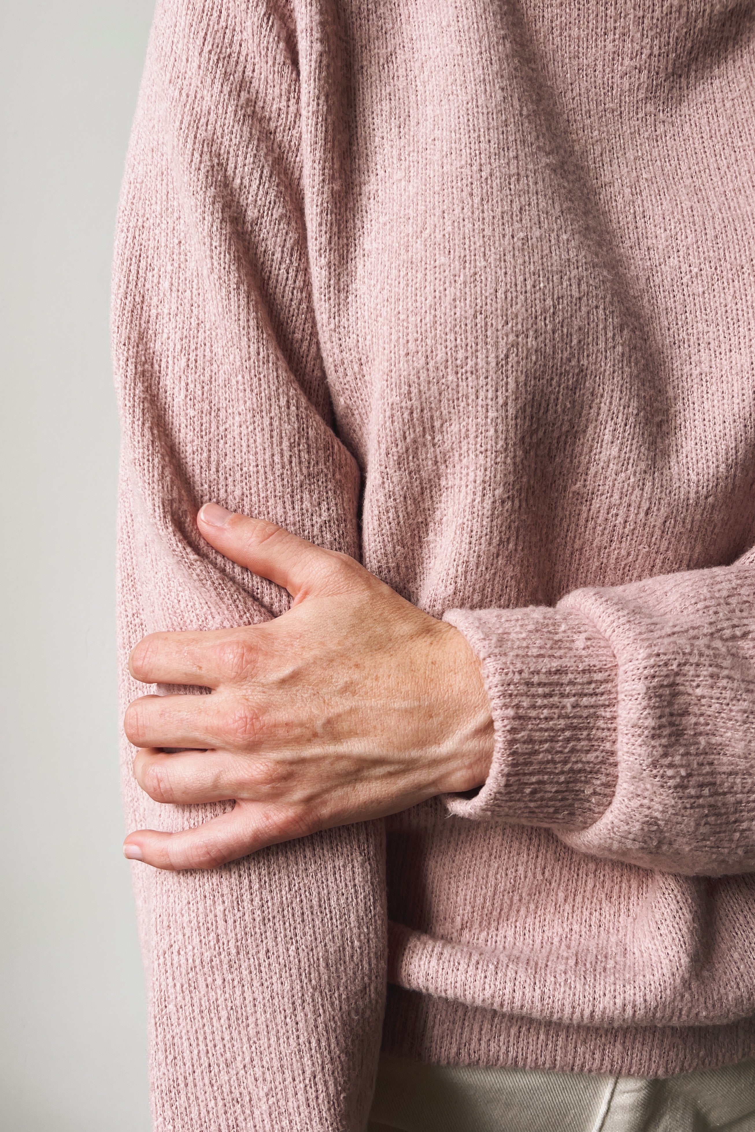 Person wearing a pink sweater with one hand on their chest to feel the softness