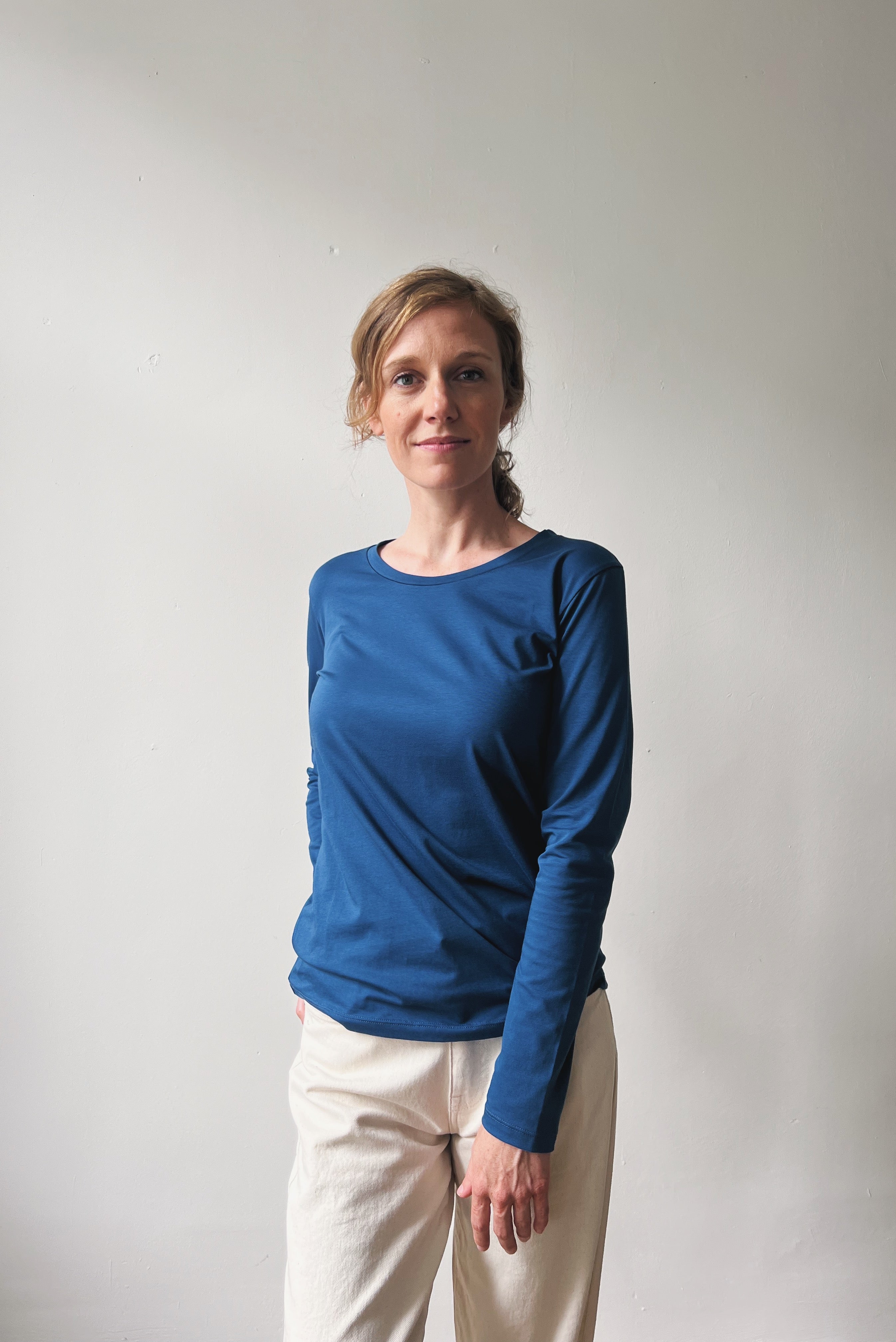 Woman wearing a blue long-sleeve shirt and oat boyfriend jeans against a plain background